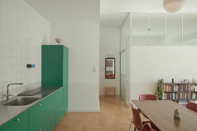 Minimalist open-plan kitchen and dining area with green cabinets and a large wooden table.