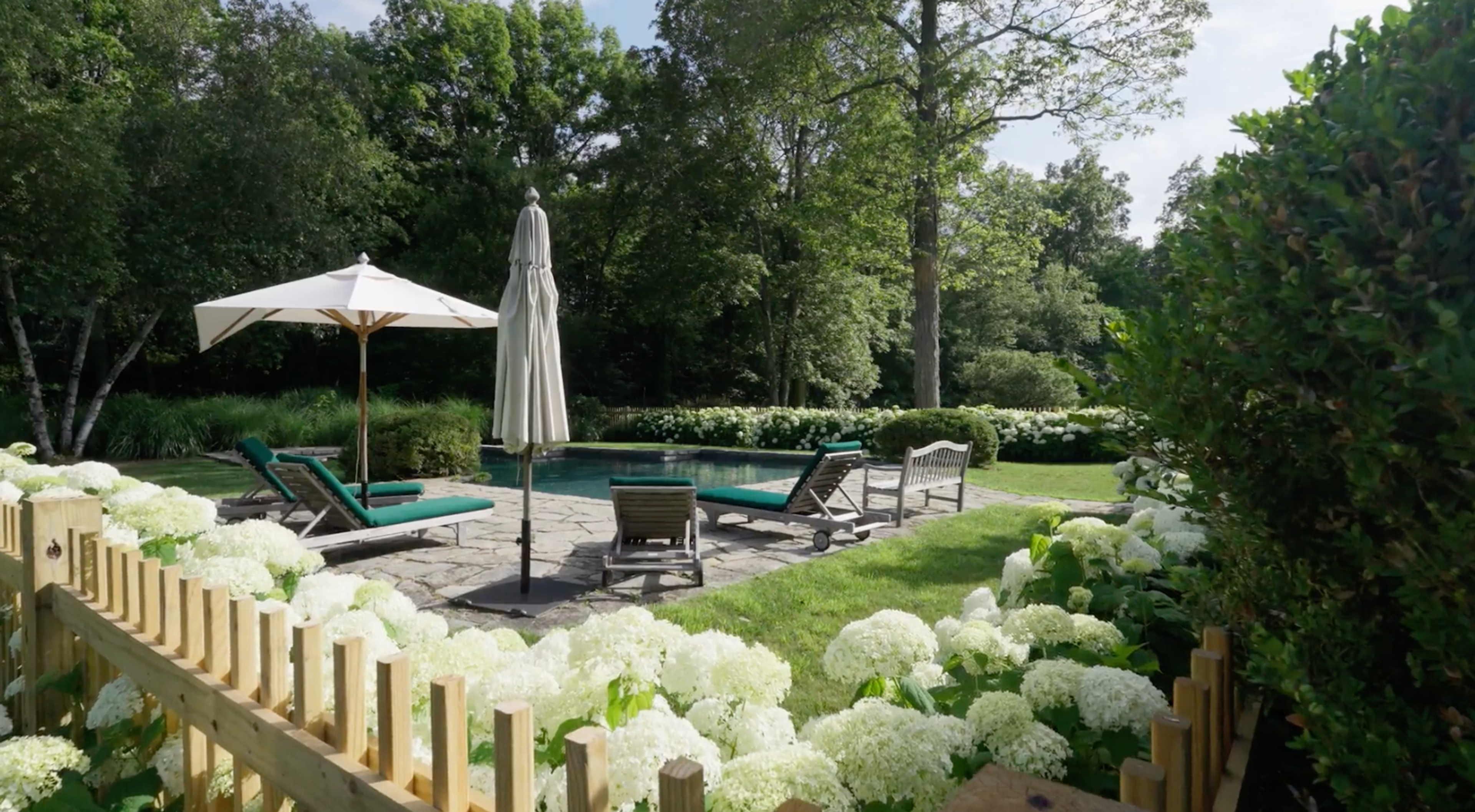An outdoor swimming pool surrounded by lush greenery and the Hudson Valley landscape.