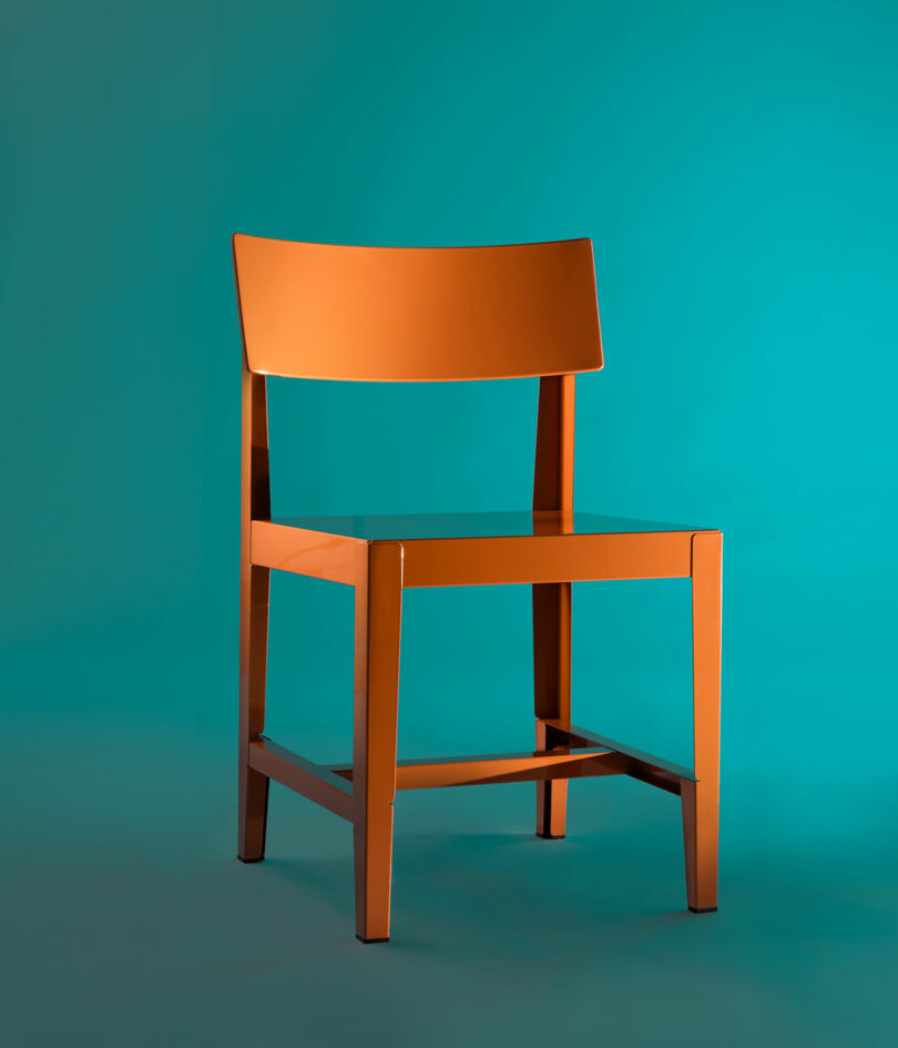 An orange metal chair with a flat seat positioned against a teal background.