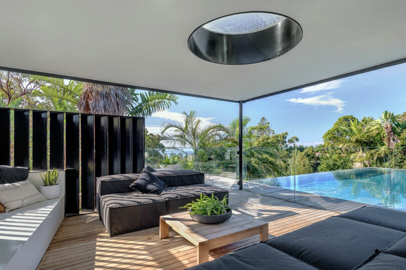Modern outdoor lounge with a sleek wooden deck and an infinity pool overlooking a lush forest canopy.