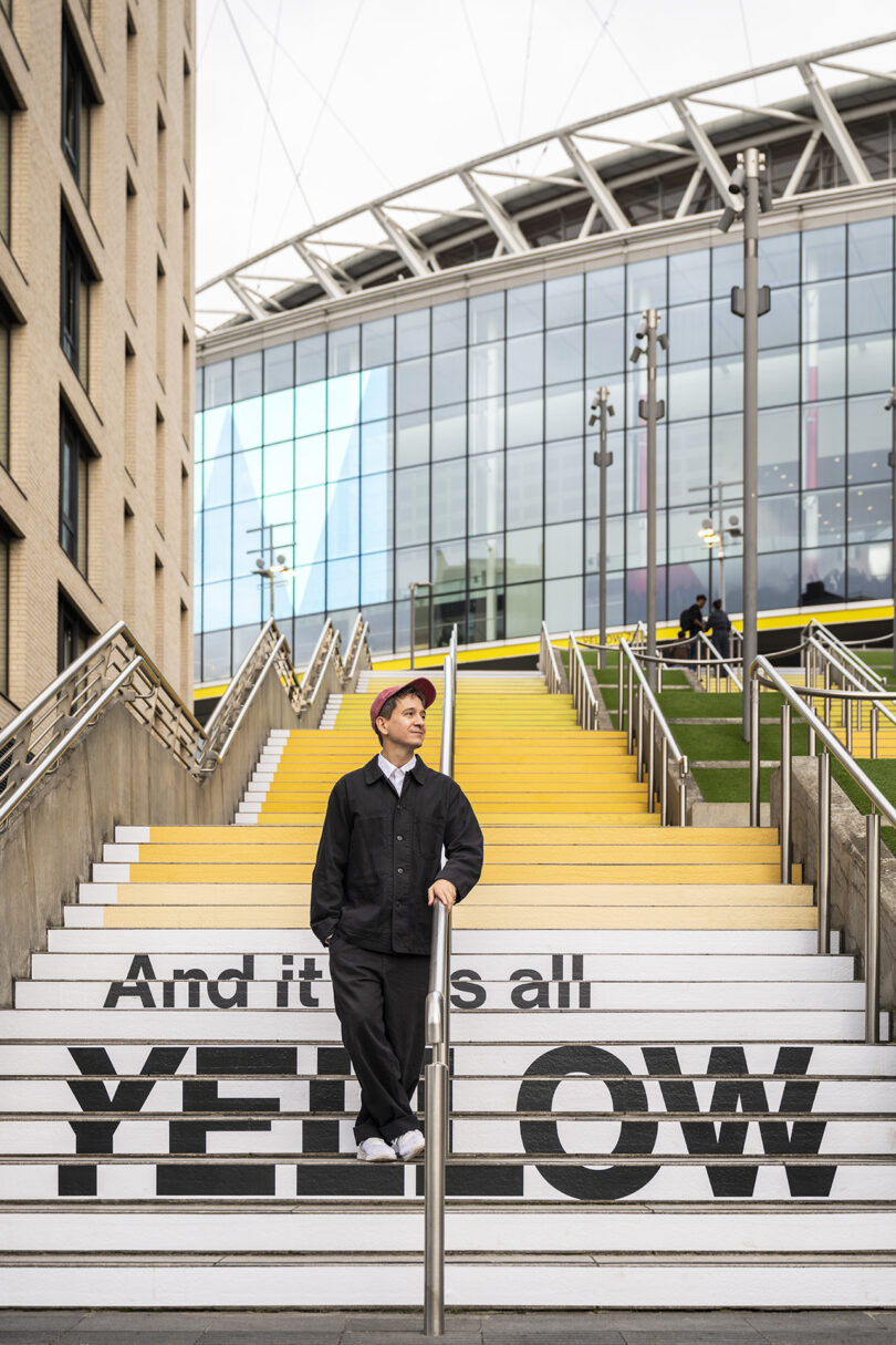 A man stands on the steps that read 'And it was all YELLOW' with the modern stadium architecture in the background.