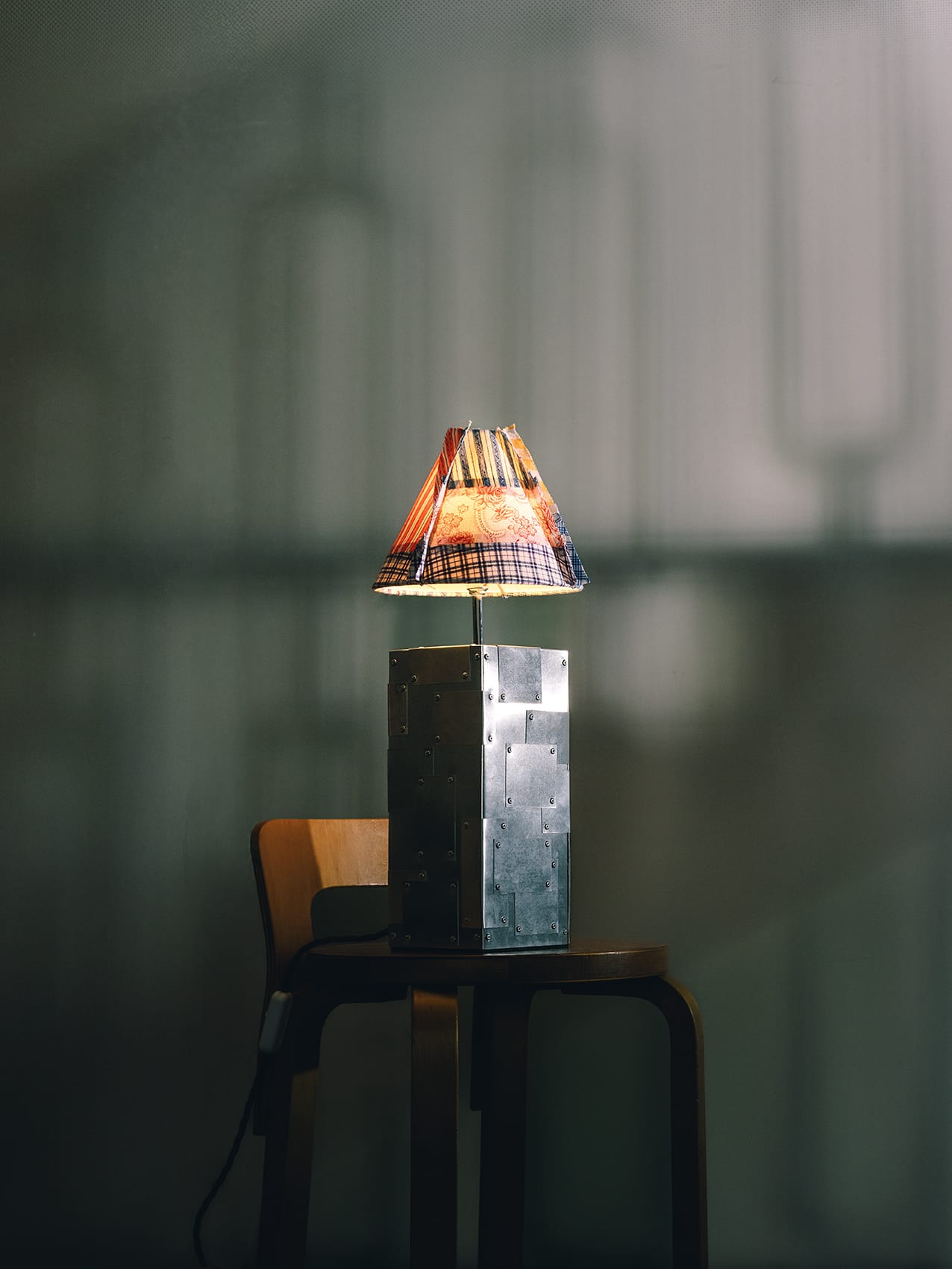 A tall artisan table lamp with a wide, structured patchwork shade and a minimalist metal stand.