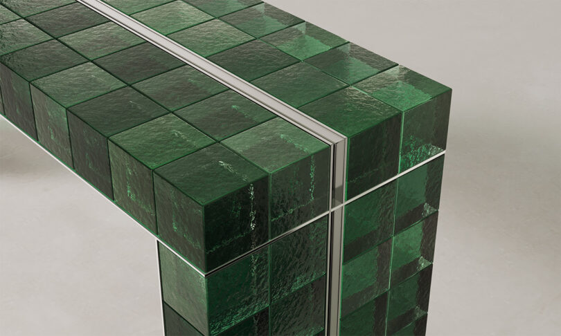 Close-up of glossy dark green glass tiles with thin metallic separation lines on a Mo.du.lo table.
