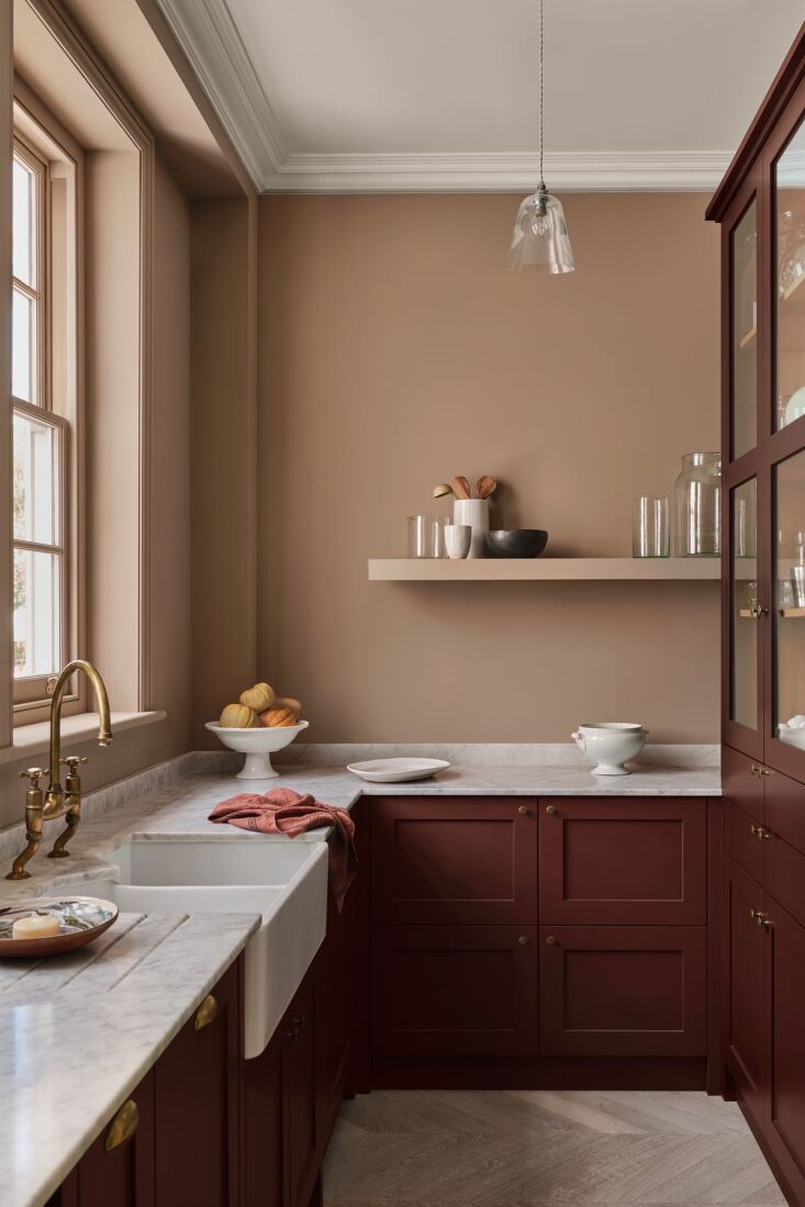 Deep red gloss cabinets in a kitchen with marble countertops and a porcelain apron-front sink.
