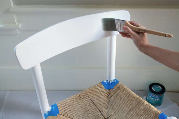 A hand applying a second thin layer of paint to a furniture piece.