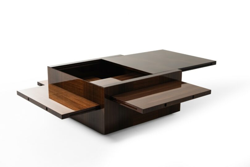 A cubic wooden coffee table with sliding checkered panels that reveal interior storage compartments.