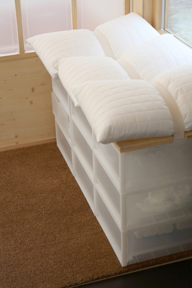 A bench made of stacked MUJI plastic storage drawers with white pillows on top