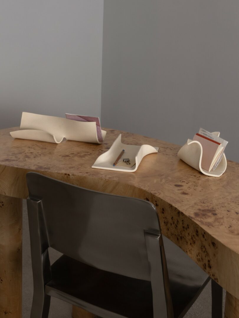 A sculptural cream-colored desk organizer set on a textured wooden desk next to a metal chair.