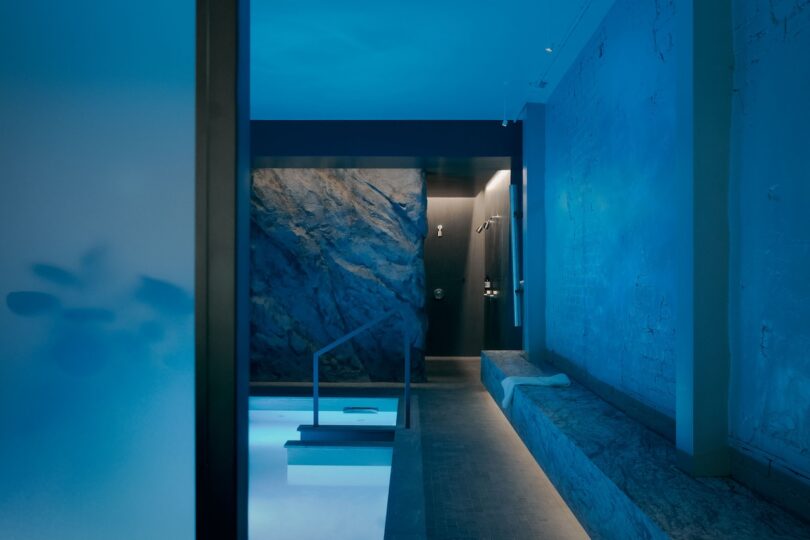 Blue-lit indoor pool with stone textures and minimalist steps.