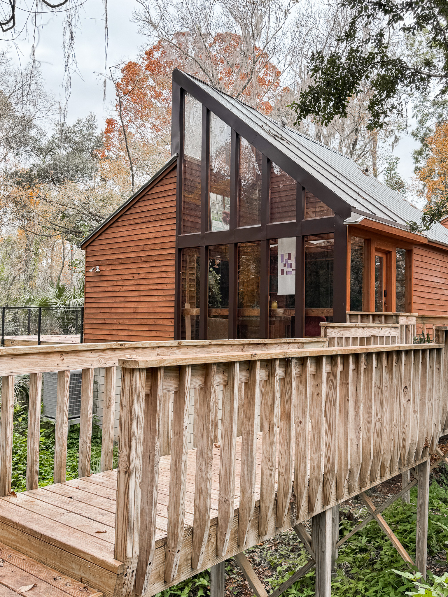 A view through the glass-enclosed greenhouse entrance featuring sharp rooflines and cedar siding.