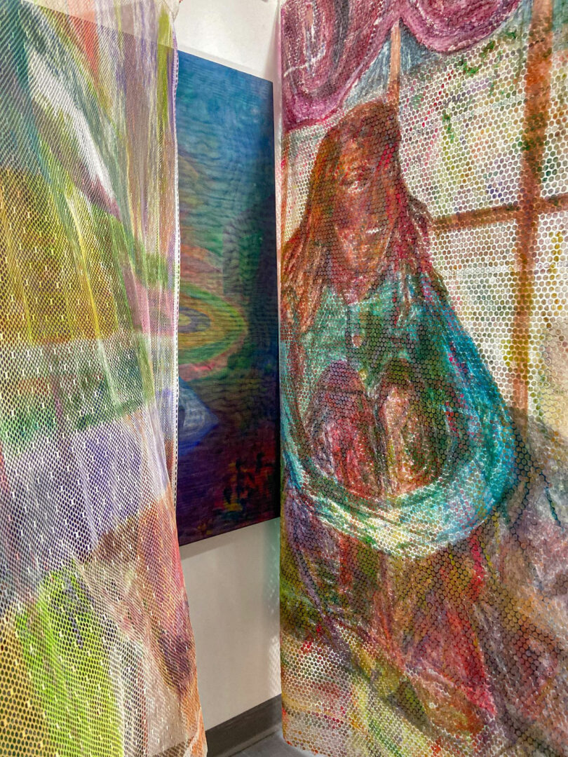 A colorful mesh curtain with a painted figure hanging near a studio window.