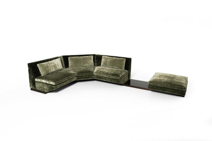 A modular green velvet sectional sofa with an integrated wooden side table and ottoman.