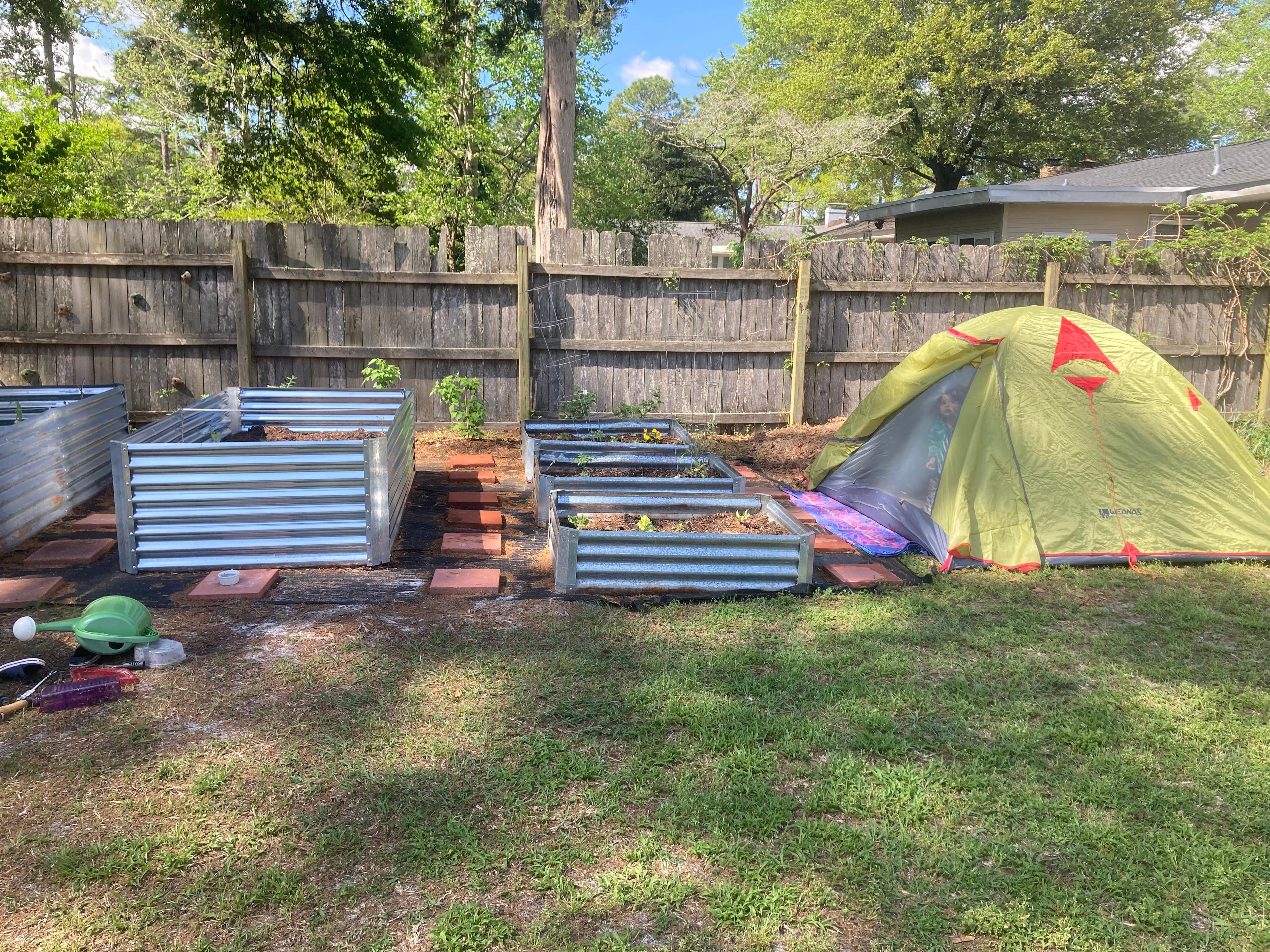 A small play tent set up in a backyard garden area near planting rows.