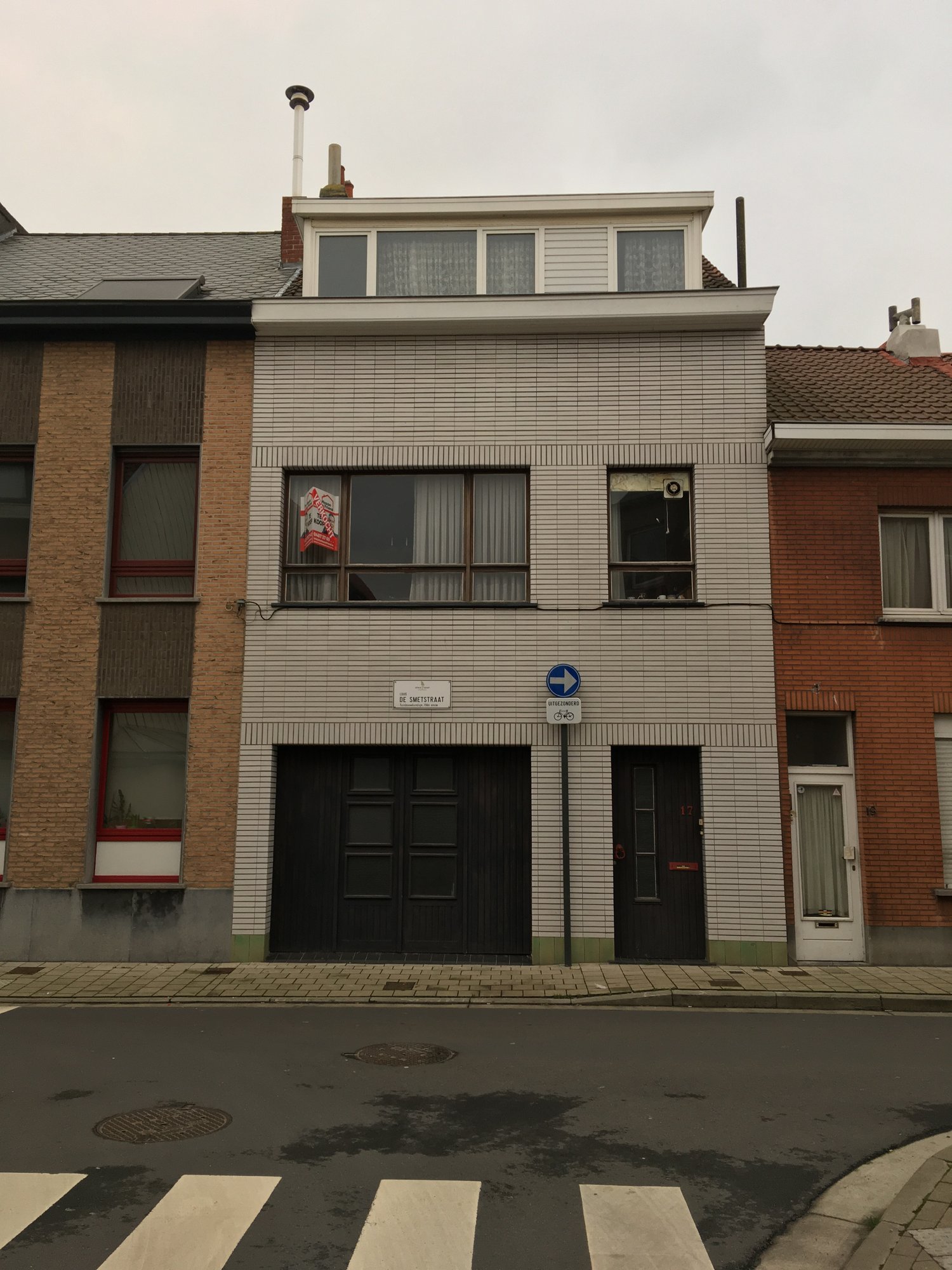 The street facade of a historic row house with glazed white brick and a new green mansard roof.
