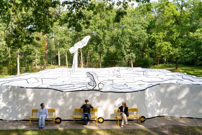 Three people sitting on yellow mobile benches in front of a large black and white abstract mural.