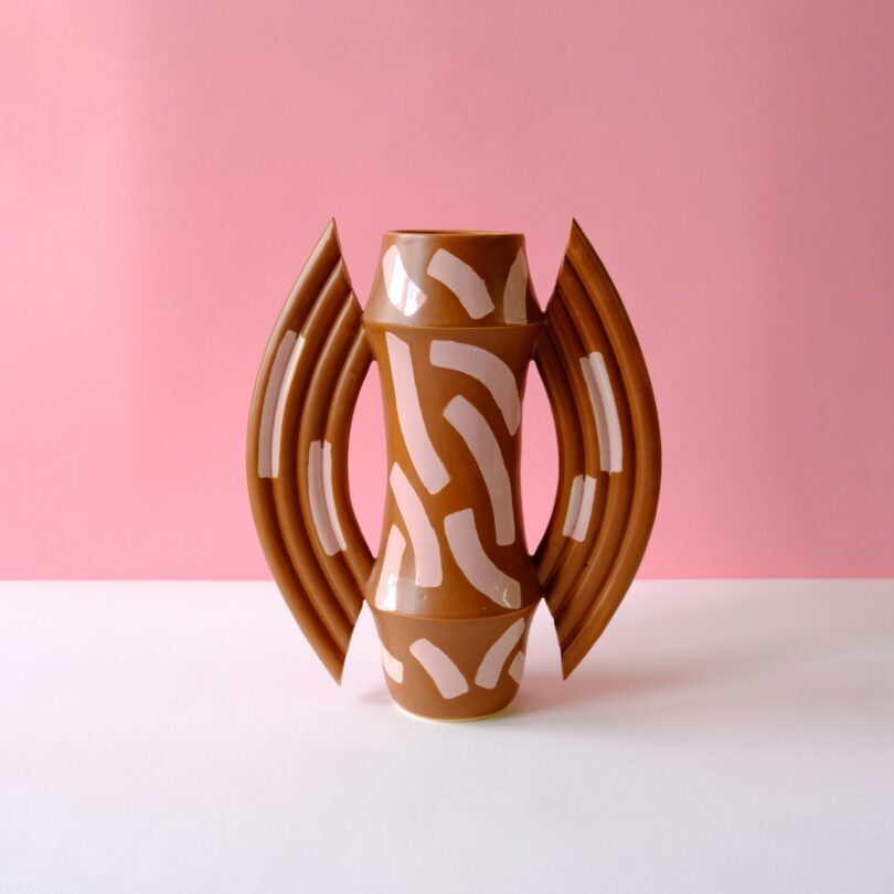 A brown artisan ceramic vase with white abstract painted patterns and symmetrical handles.
