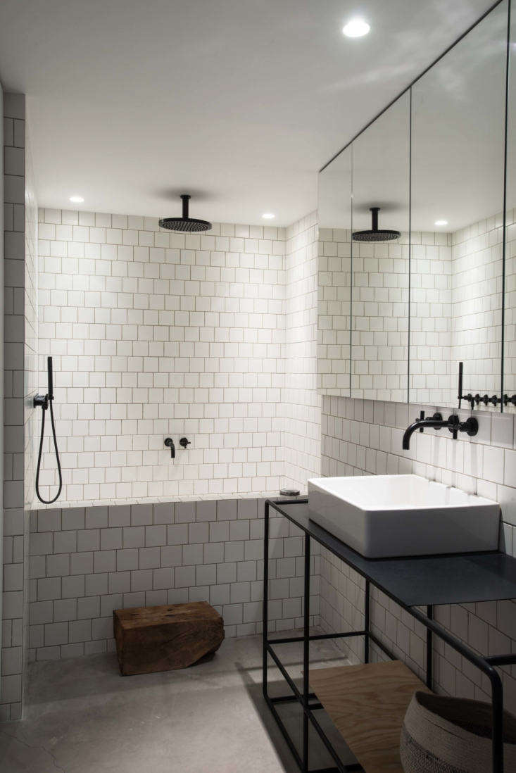 Modern master bathroom with white square tiles, a custom steel sink frame, and black industrial faucets.