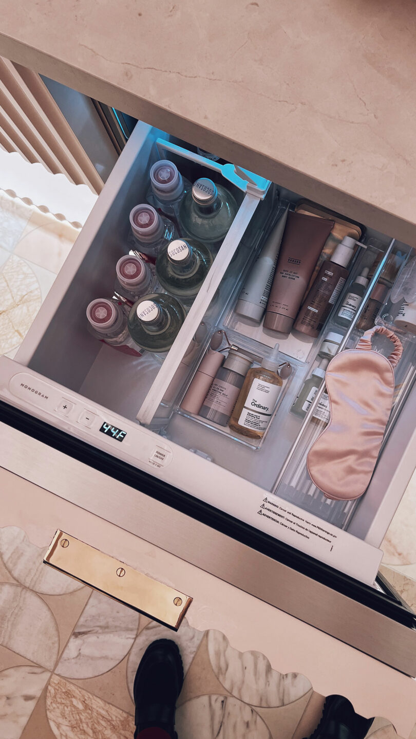 A kitchen drawer organized with skincare bottles, drinks, and a sleep mask.
