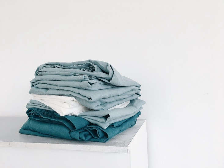 A stack of linen sheets and pillowcases in various shades of blue and green.