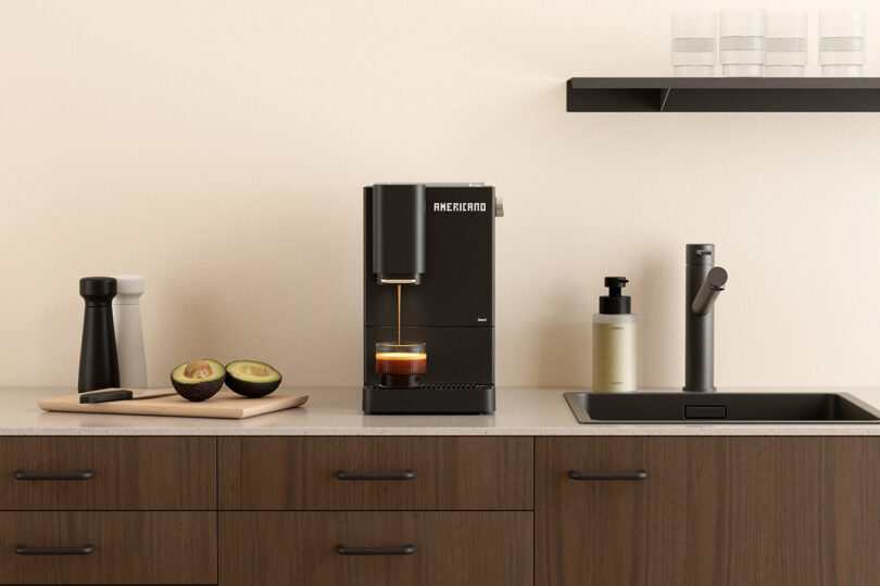 A coffee machine brewing coffee on a kitchen counter next to a cutting board with an avocado and a sink.