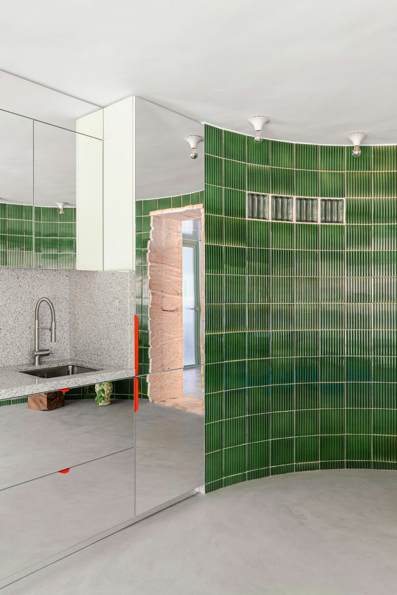 Modern kitchen setup with glossy green vertical tiles and stainless steel fixtures.