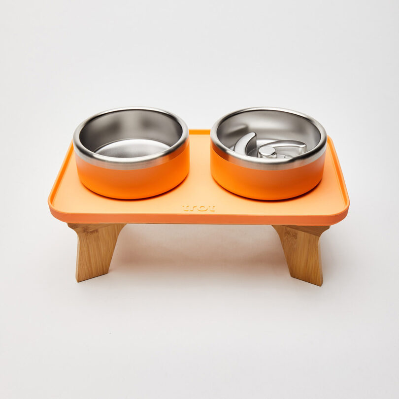 An orange elevated dog feeder with a stainless steel bowl and a spiral-patterned slow-feed insert.