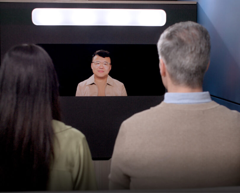 A woman and man looking at a life-size digital representation of an Asian man on an Ocular View screen under soft, oblong lighting.