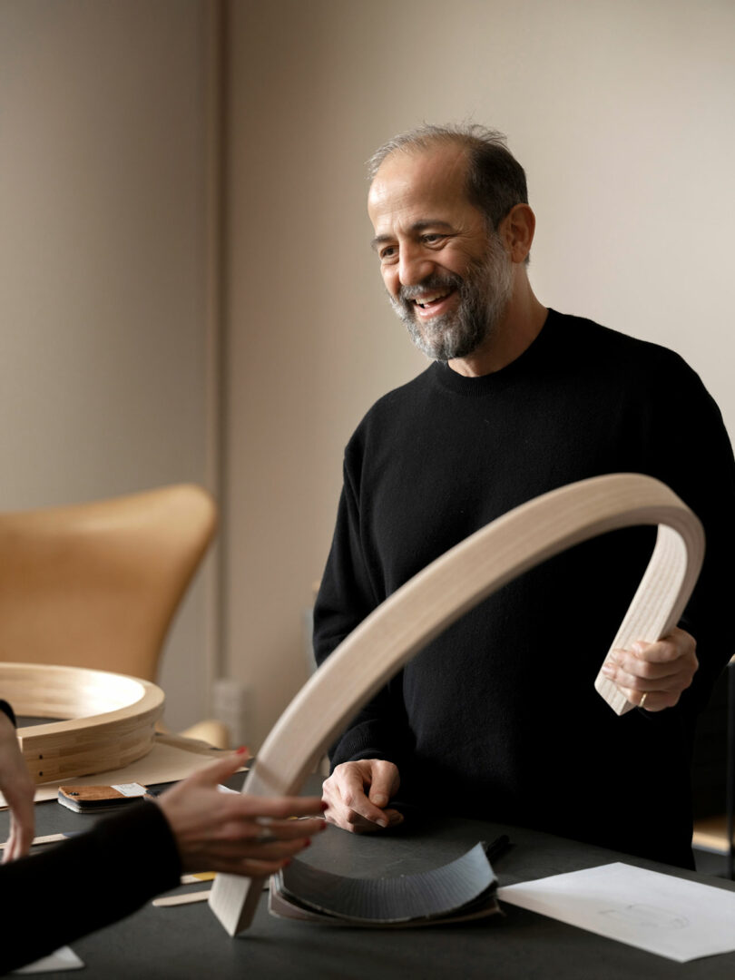 Designer Michael Anastassiades working with a curved wooden chair component in a studio.