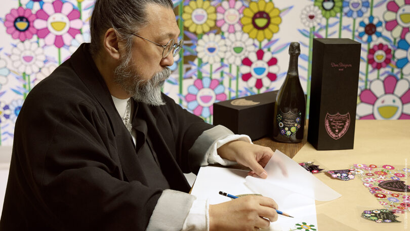 Takashi Murakami sketching colorful flowers at a table with champagne bottles.
