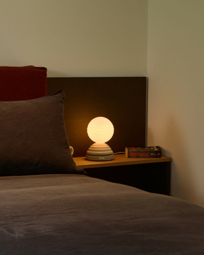 A cozy bedside setup with a wooden nightstand, a book, a mug, and a warm lamp.