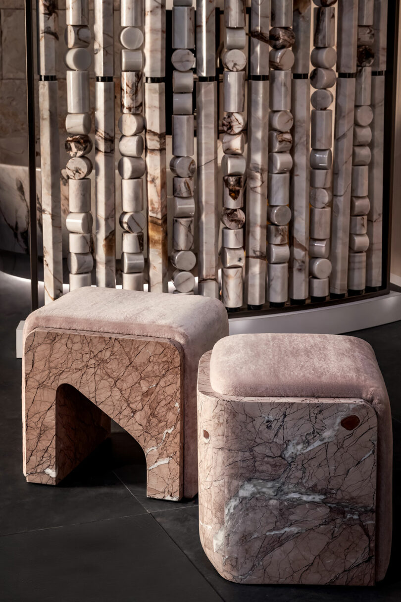 Two geometric marble stools or ottomans displayed on a dark floor with a decorative stone backdrop.