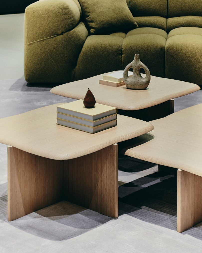 Close-up of wooden coffee tables with books and a vase placed in front of a green upholstered sofa.