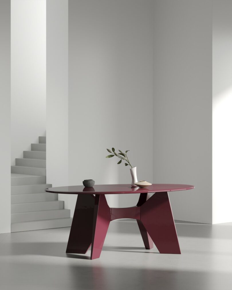 Round maroon table with a high-gloss finish standing in a minimalist room near a white staircase.