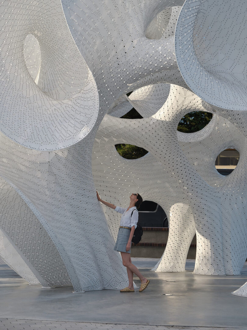 A person standing inside the Orb looking up through the perforated canopy at the sky.