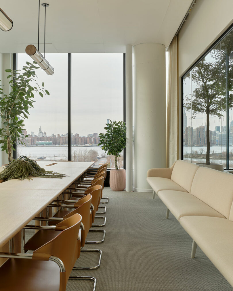 Minimalist conference room with a long table and large windows offering an expansive view of the East River and skyline.