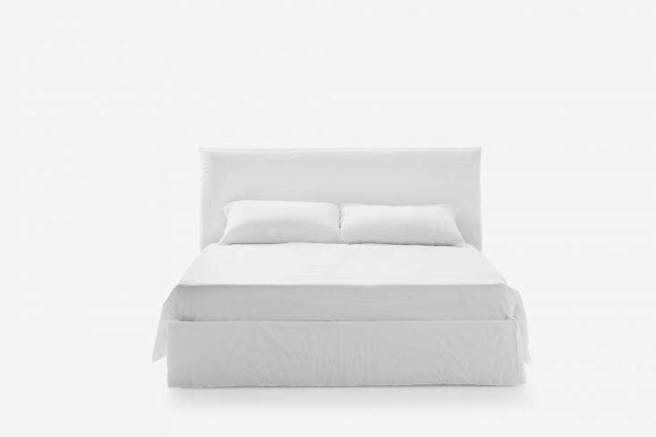 A slipcovered bed in white cotton upholstery within a minimalist room.