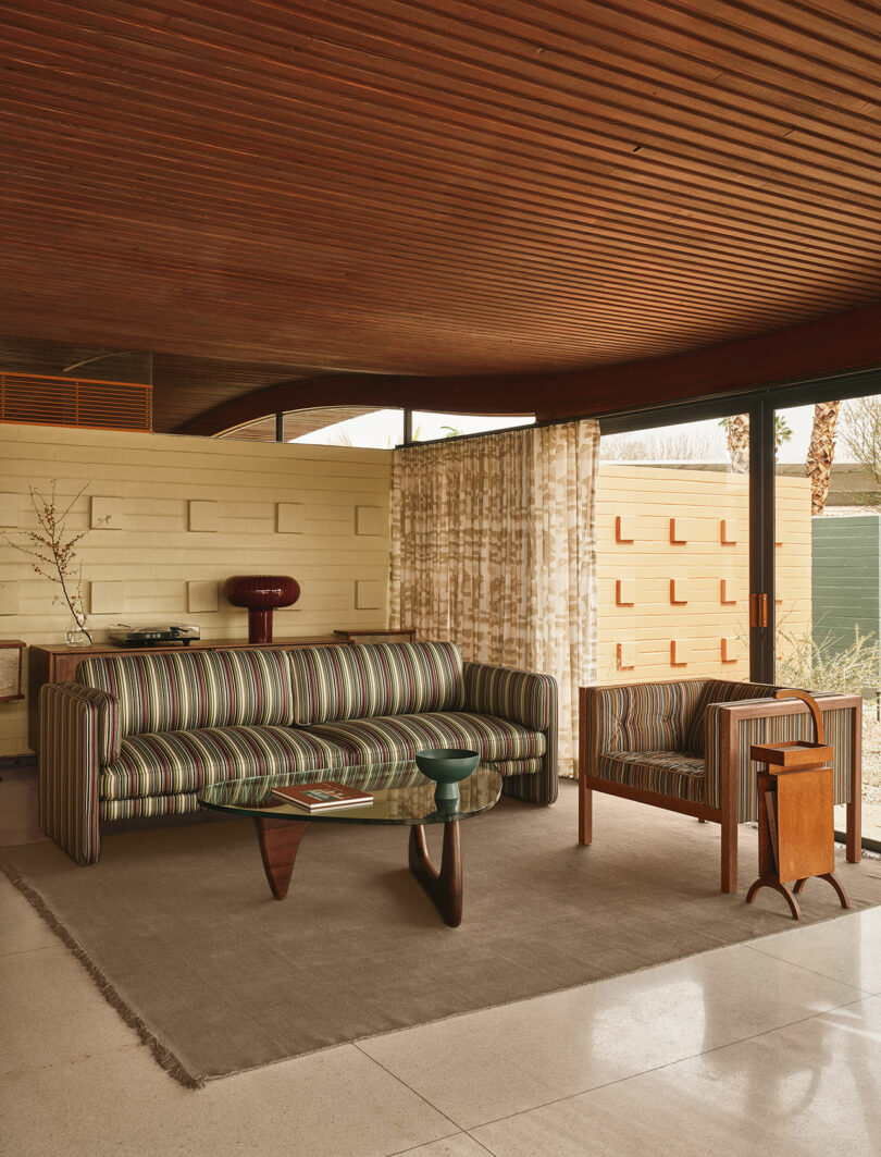 A mid-century modern living room featuring a Paul Smith striped sofa and large glass windows.