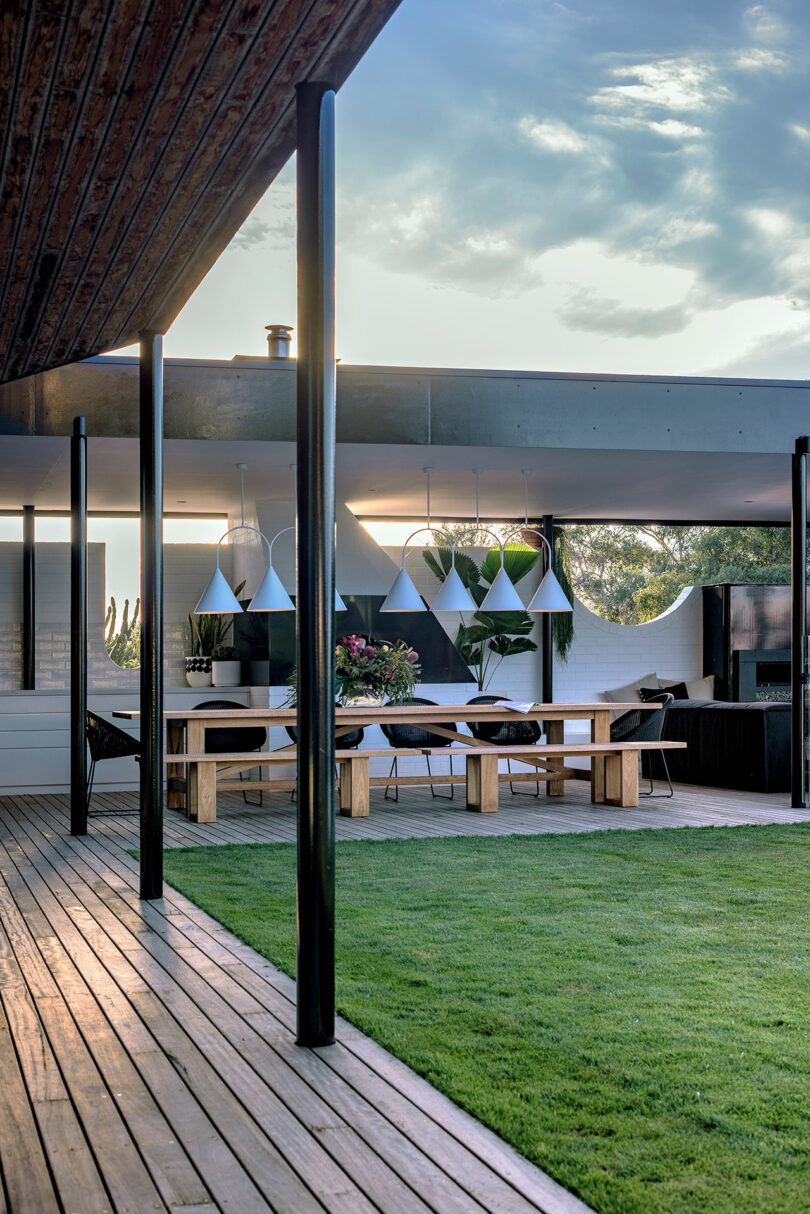 A modern patio featuring stone flooring, black structural pillars, and a clean-cut lawn area.
