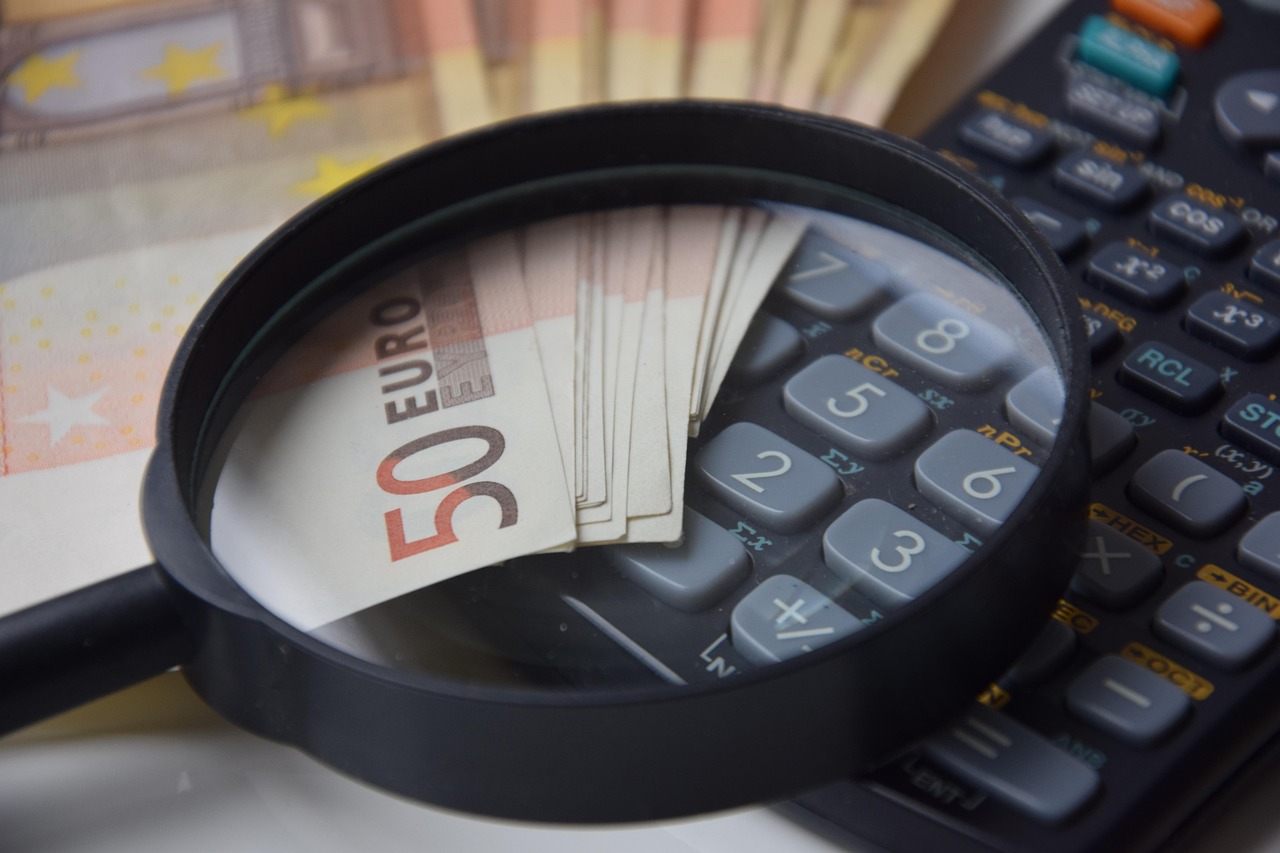 A person using a calculator and notepad on a kitchen counter near an appliance.