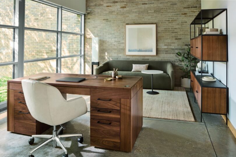 A Lincoln desk in a modern office with a brick wall, white swivel chair, and natural lighting.