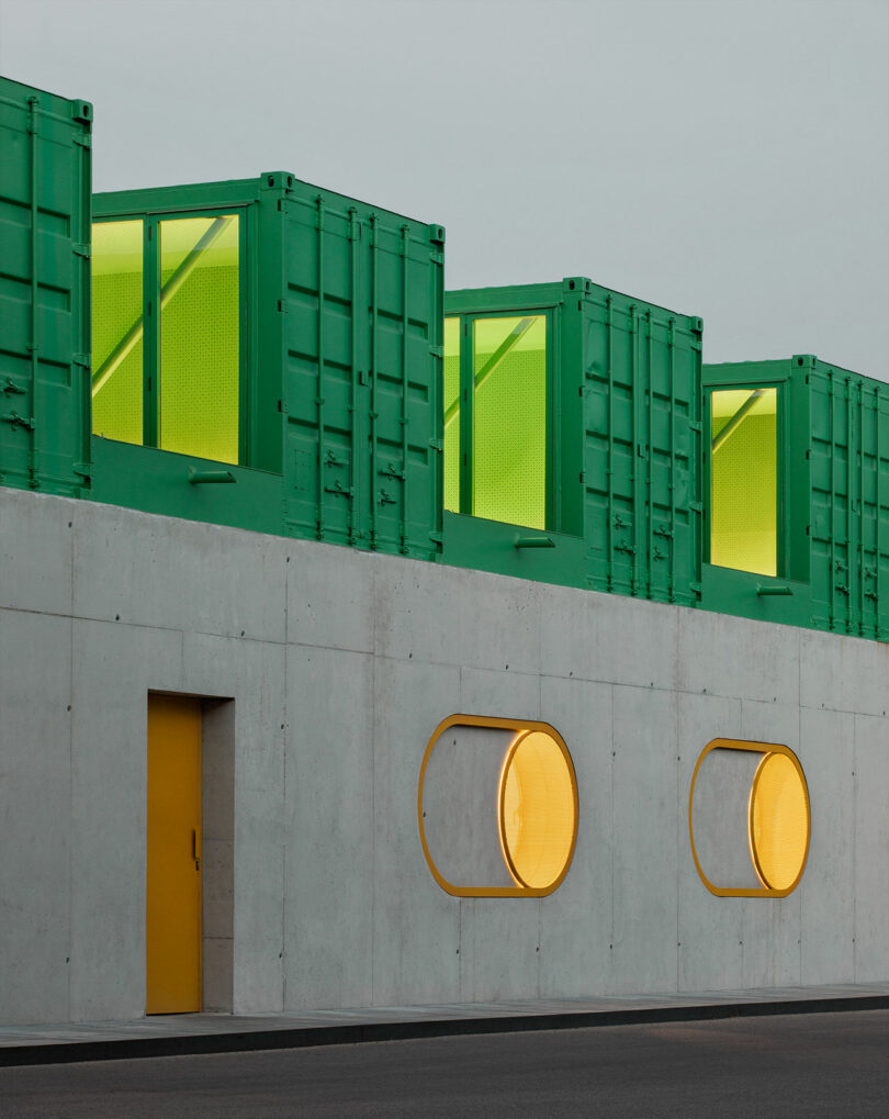 Building with a gray concrete base and stacked green shipping containers on the roof.