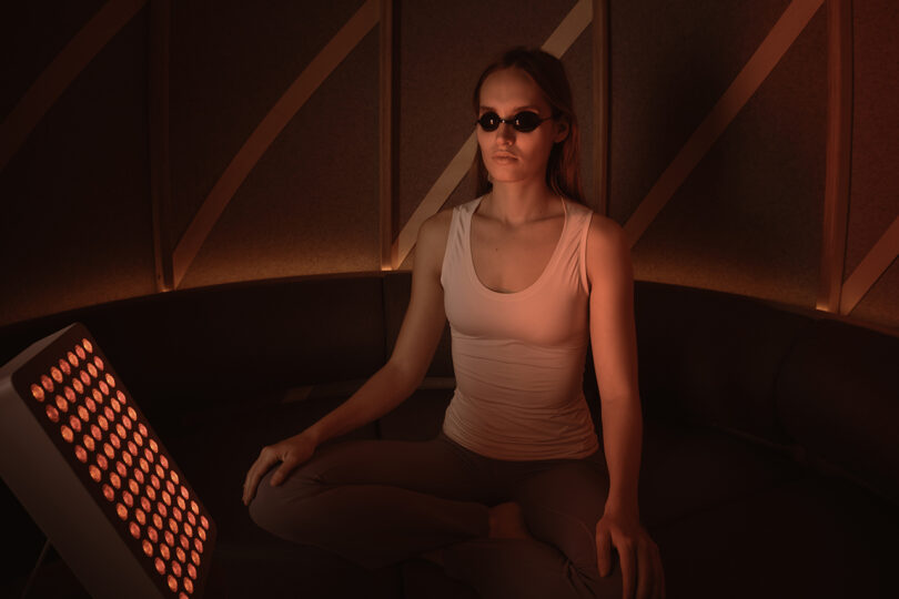 A person sitting in a dimly lit space illuminated by a red light therapy panel.