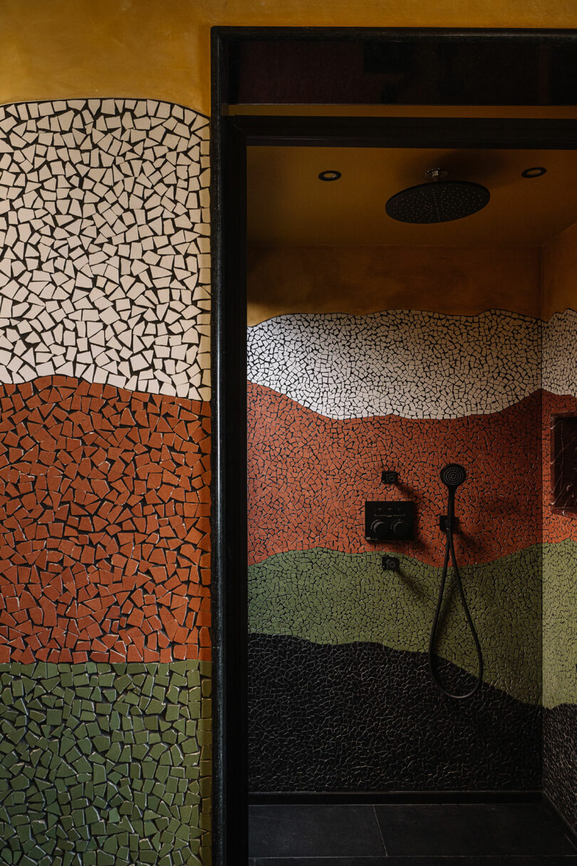 A close-up of a mosaic tile wall featuring flowing patterns of earthy reds, greens, and blacks.