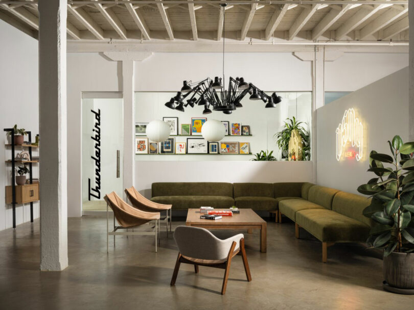 A modern office lounge with green sofas, a neon 'Howdy' sign, and geometric lighting.