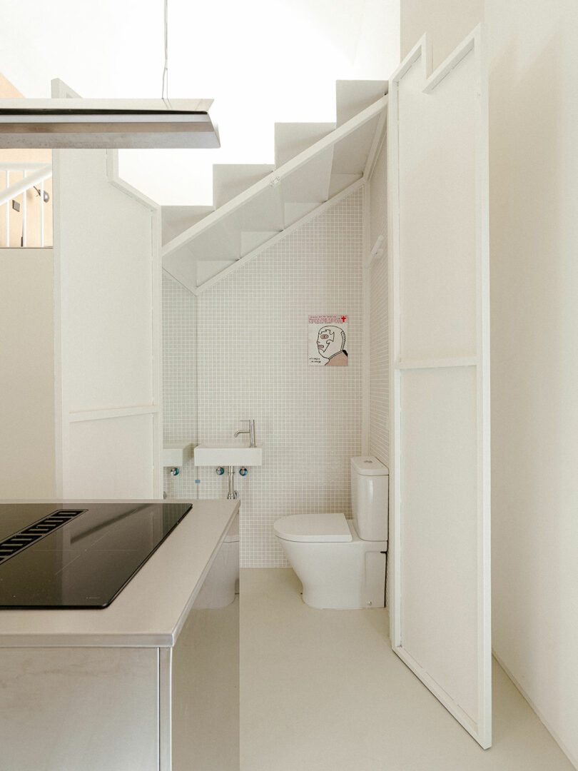 A small, minimalist bathroom tucked neatly under a white staircase.