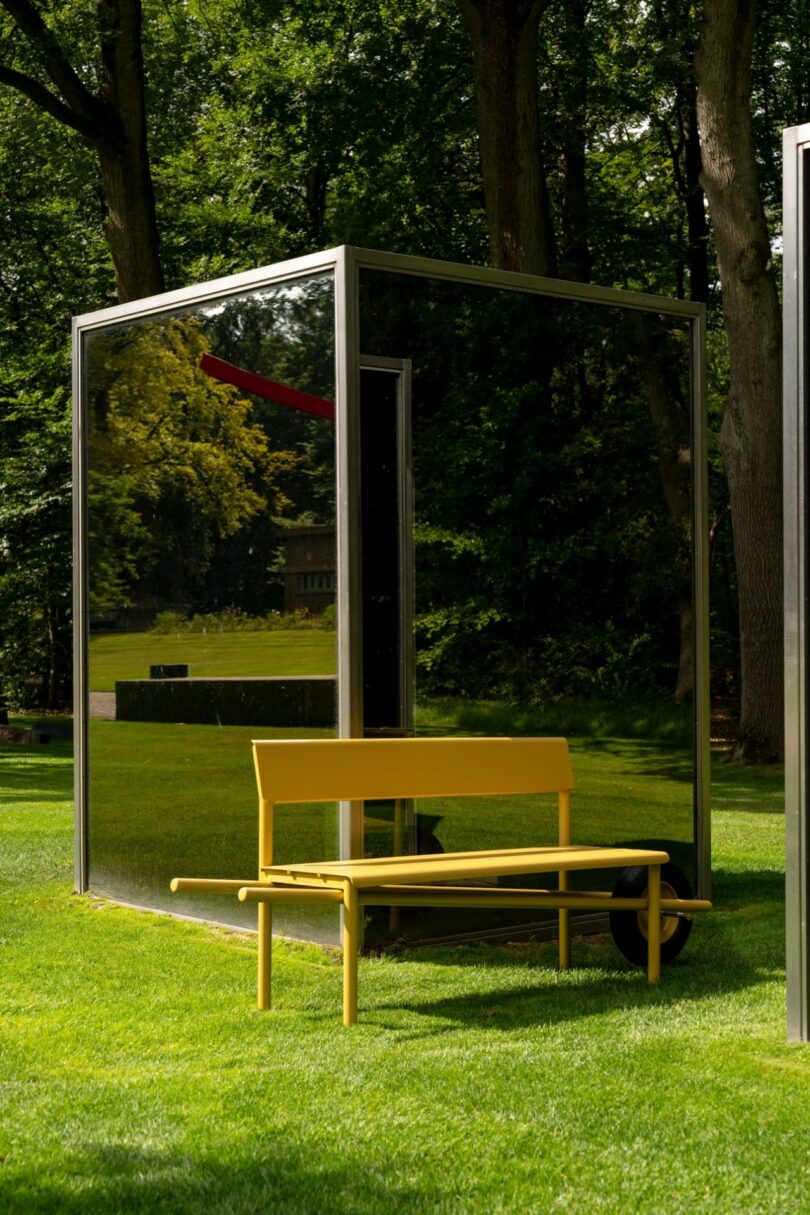 Yellow bench on green grass in front of a modern glass and steel structure.