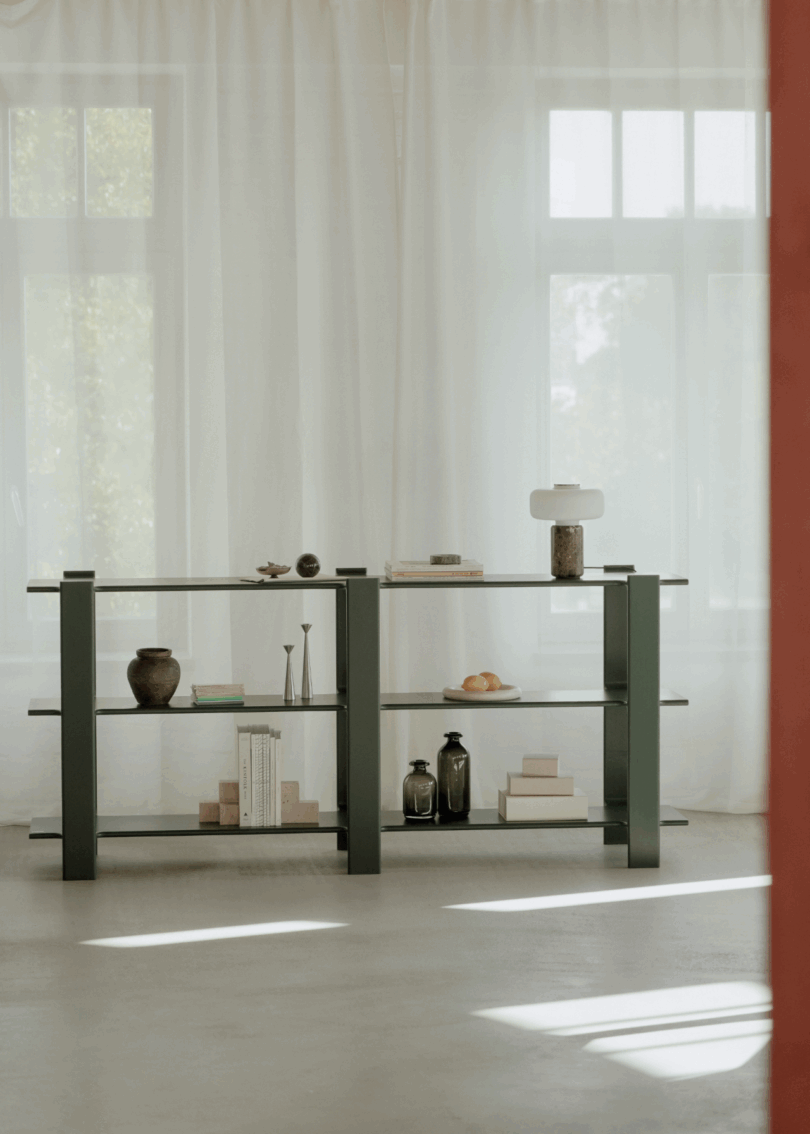 Large minimalist wooden bookshelf featuring various decor items against a backdrop of sheer white curtains.
