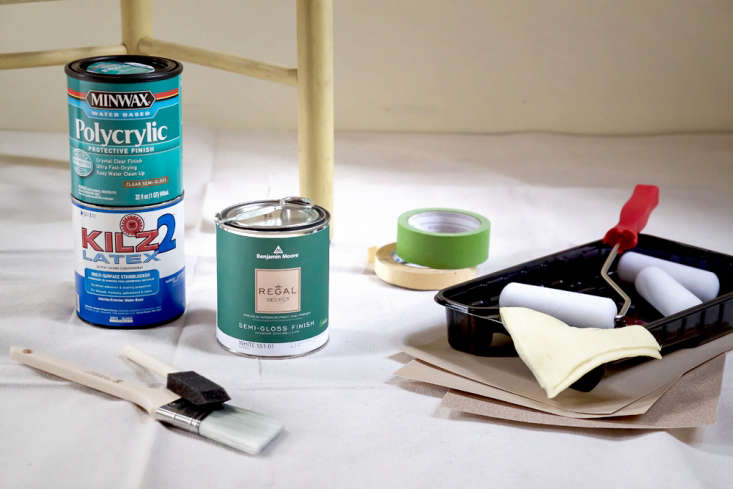 A collection of paint cans, brushes, and rollers laid out for a furniture project.