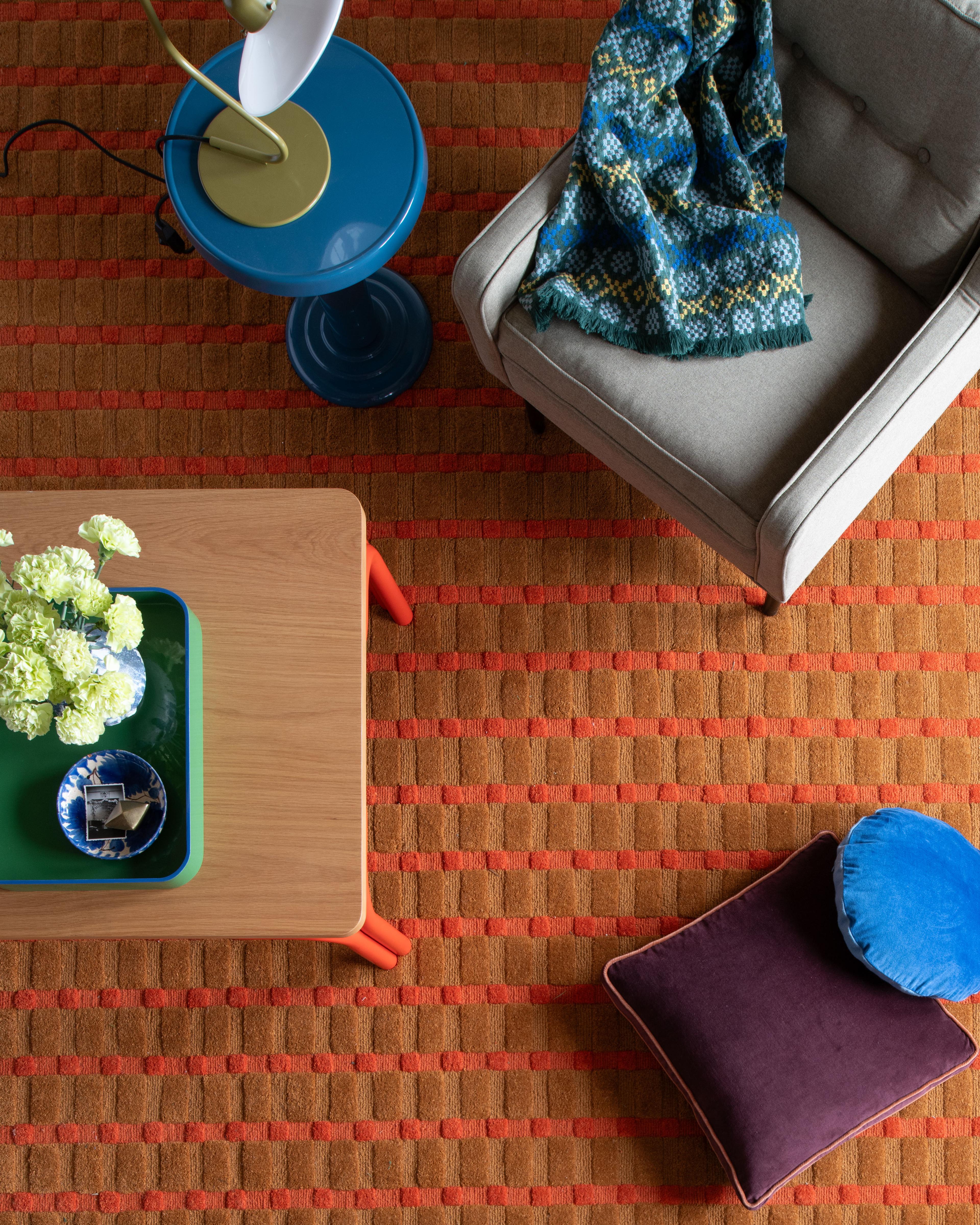 Overhead view of a living room featuring a textured rug, wooden stool, and layered throw blankets.