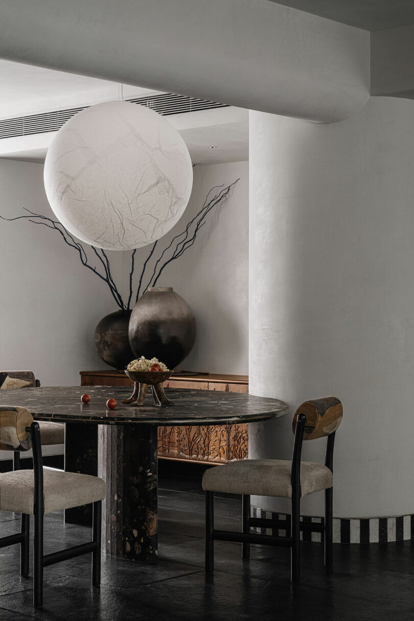 A minimalist dining room with white walls, a round black table, and a large spherical pendant light.